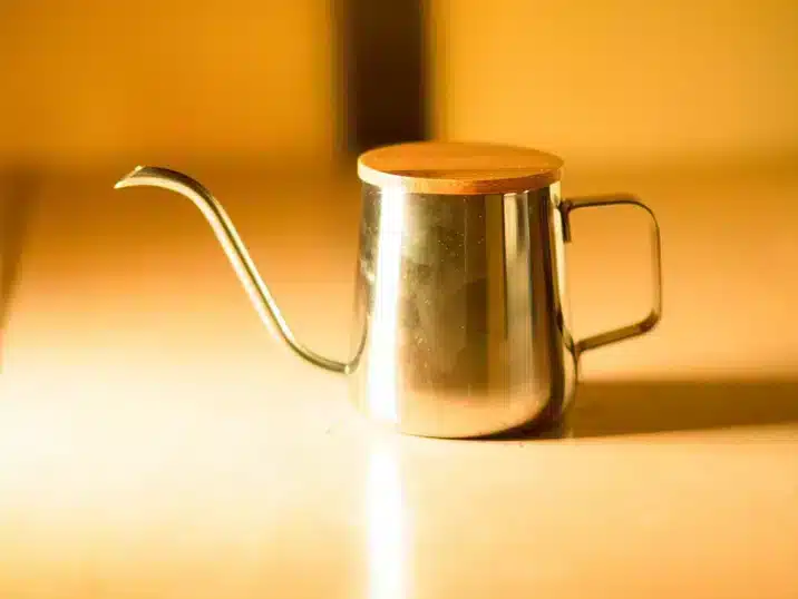 Een goudkleurige metalen gieter met houten deksel