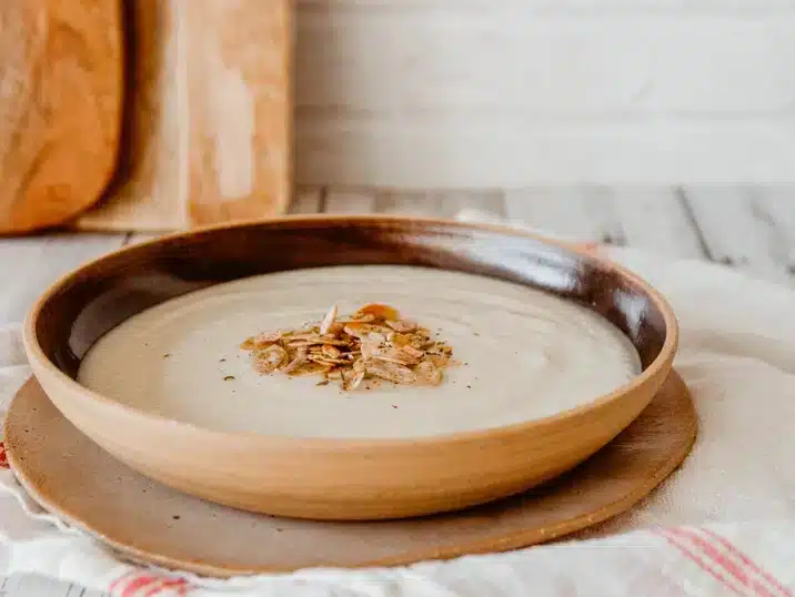Een keramieken soepkom met daarin soep en geroosterde amandelschilfers