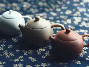 Een rode, bruine en witte theepot van keramiek op een gebloemd tafelkleed