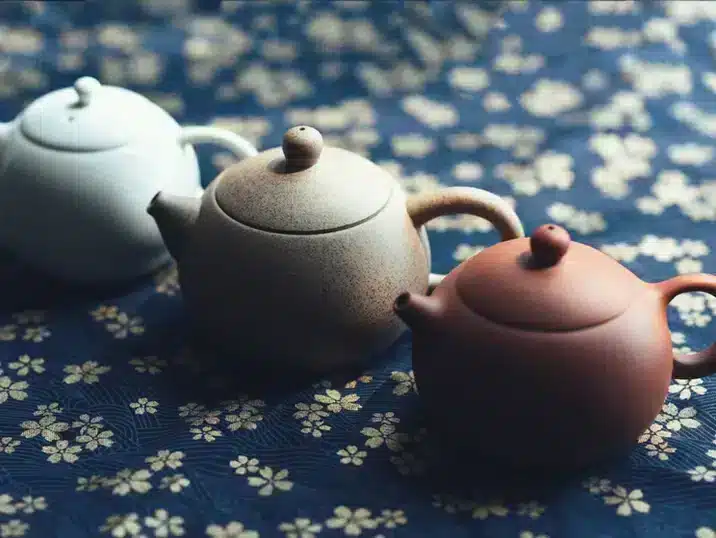 Een rode, bruine en witte theepot van keramiek op een gebloemd tafelkleed