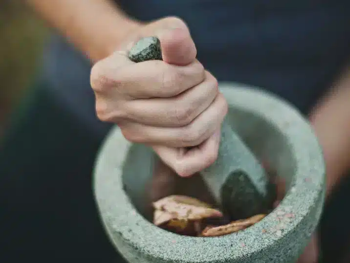 Hand die met de stamper in de vijzel kruiden maalt
