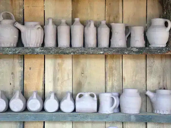 Verschillende gieters en kannen op een houten plank, gemaakt van klei