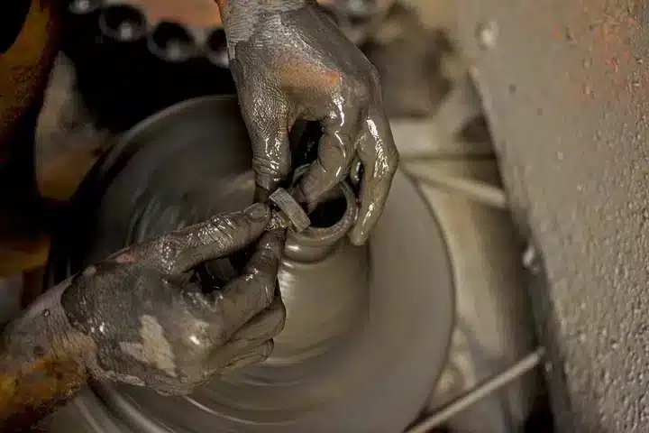 Een detail van handen die een fles uit zwarte klei kneden en draaien op de draaischijf