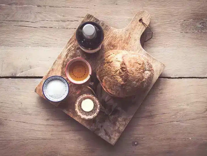 Een houten plank met daarop brood, zout en een keramieken oliefles