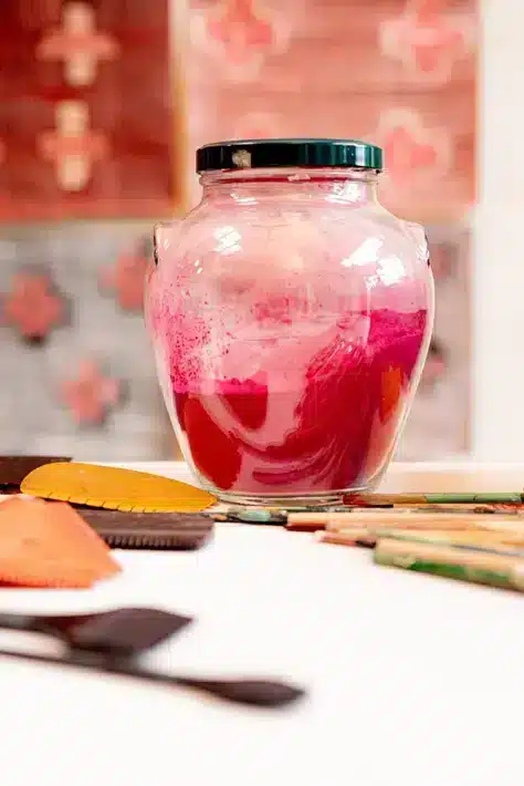 Een bokaal met rood keramisch pigment en wat klei tools op een tafel