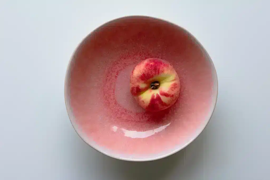 Is glazuur gevaarlijk? Een fruitschaal van keramiek met rode glazuur en daarin een perzik