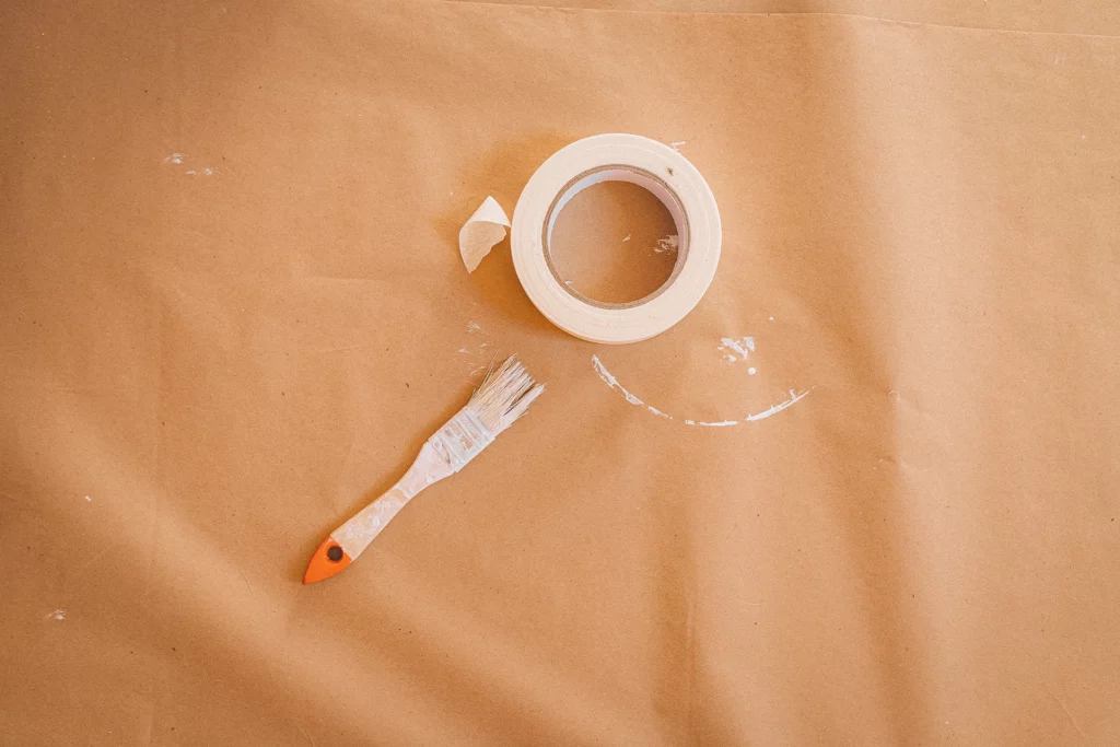 Rol witte schilderstape en verfborstel op ondergrond van bruin papier